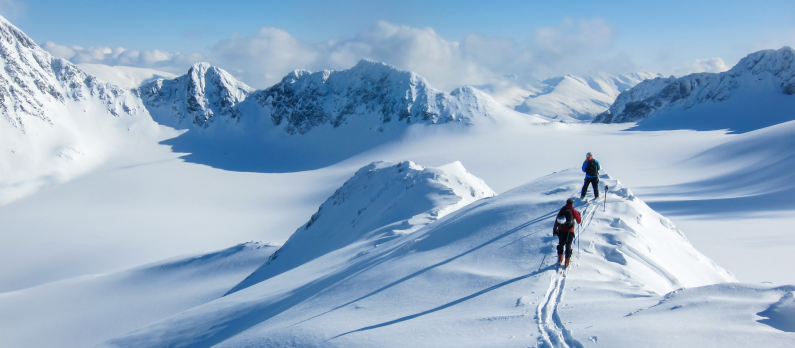 To personer går på ski på snødekt fjell