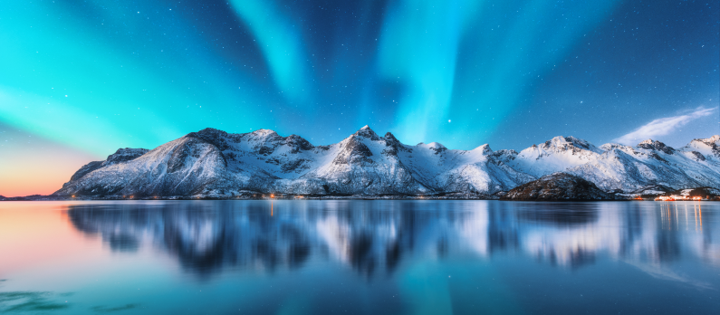 Vinterbilde av et snødekt fjell med nordlyset på himmelen som speiler seg i vannet