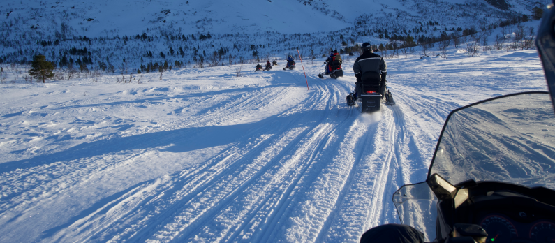 En gruppe på snøscootertur med et fjell i bakgrunnen