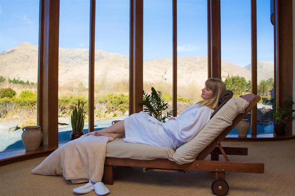 Woman lies on deck chair in spa looking out at mountains