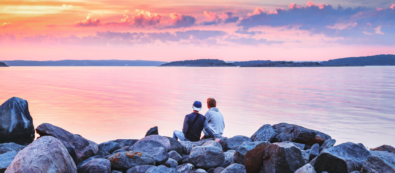 Male_couple_sitting_on_stones_at_sea_shore